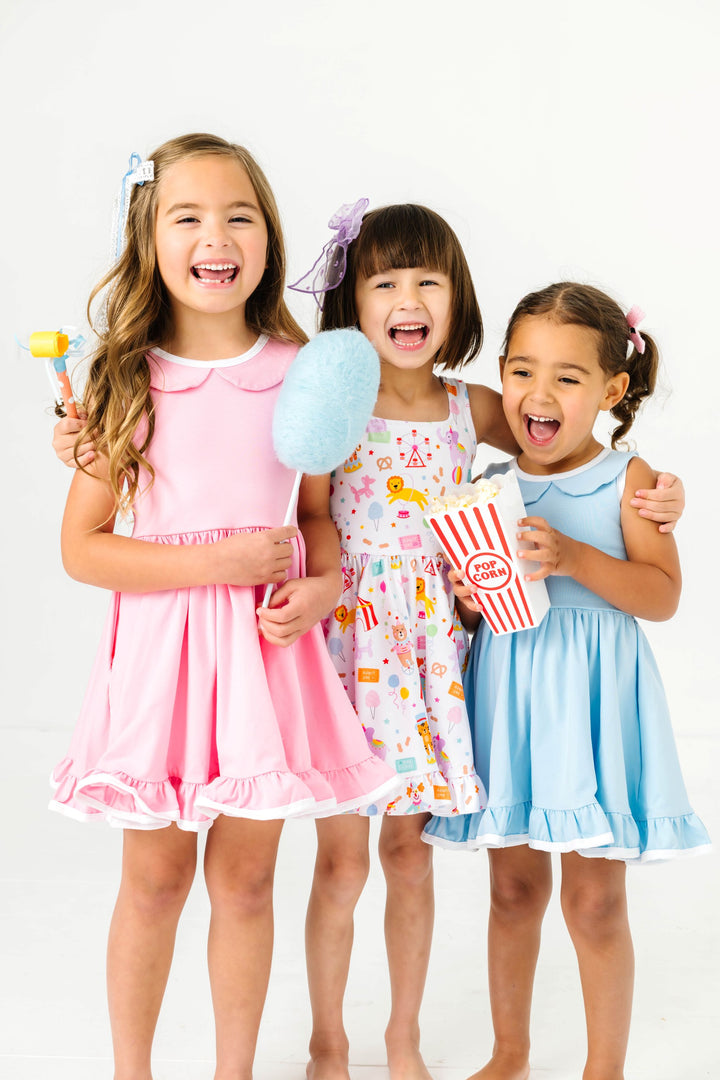 little girls in coordinating pink, blue and circus print sleeveless twirl dresses with popcorn and cotton candy