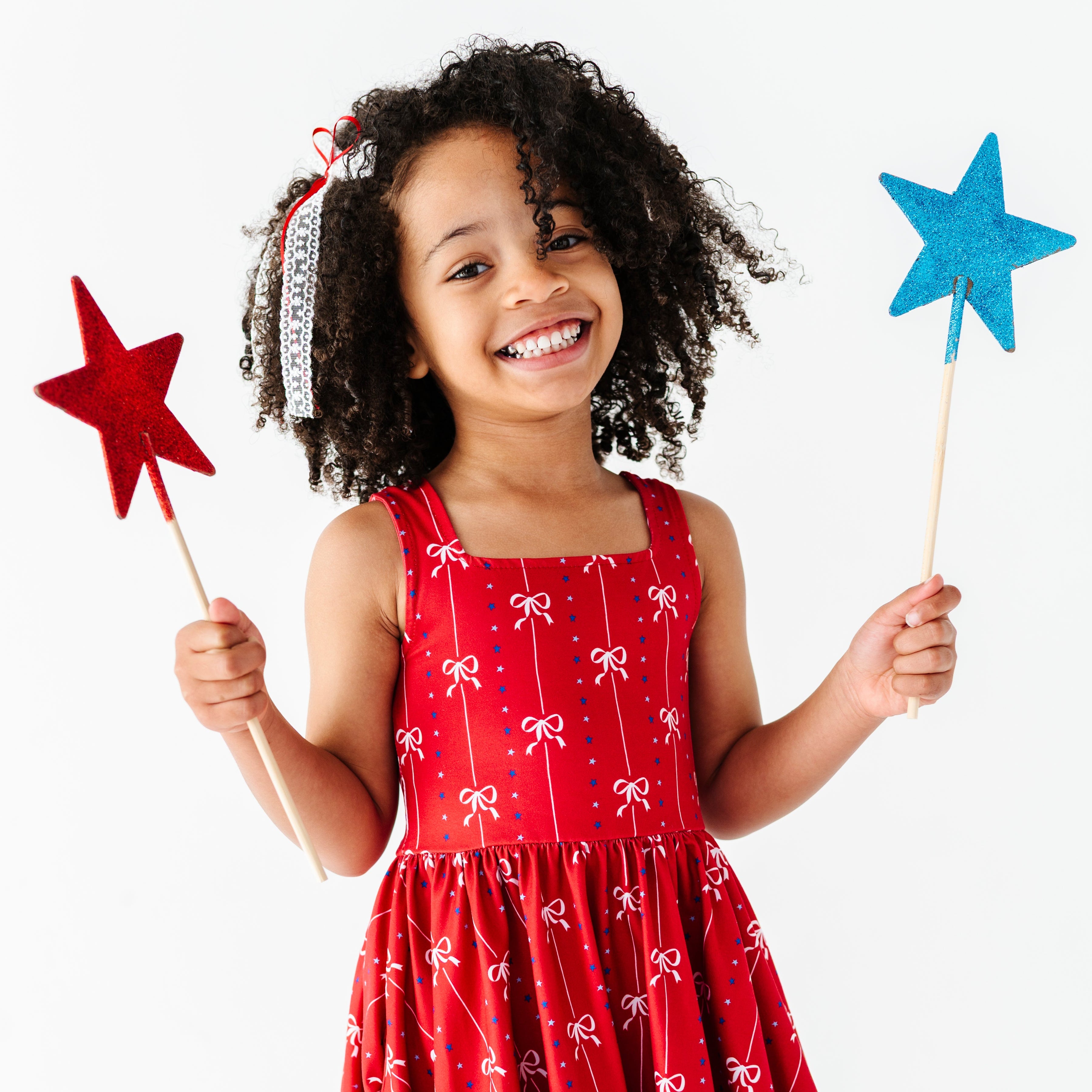 little girl holding star decorations in red sleeveless twirl dress with petite white bow and blue star print