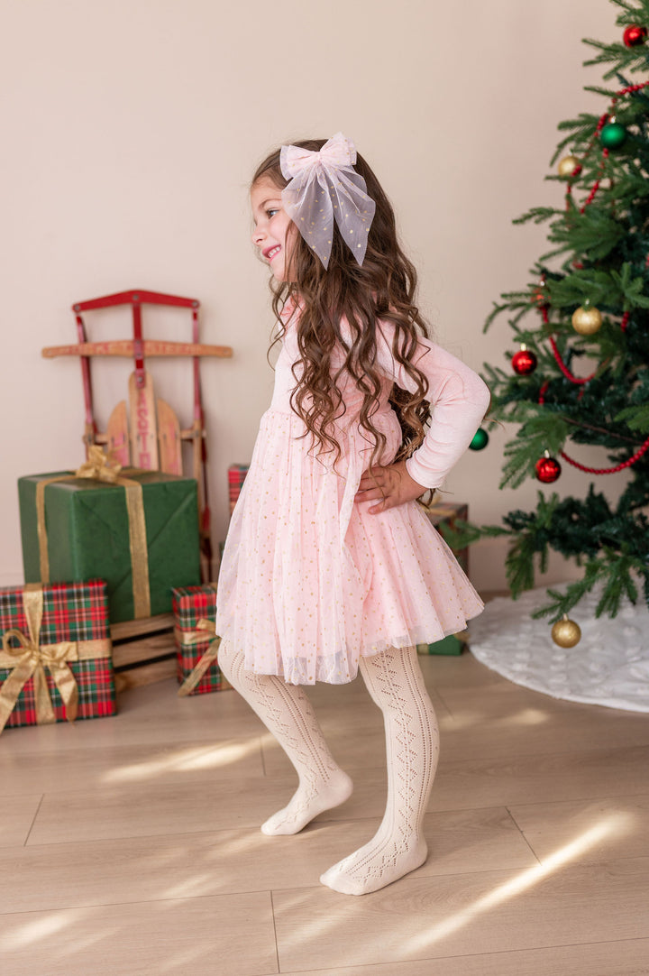 girl wearing pink fancy christmas dress with sparkly gold dotted tulle skirt and matching hair bow