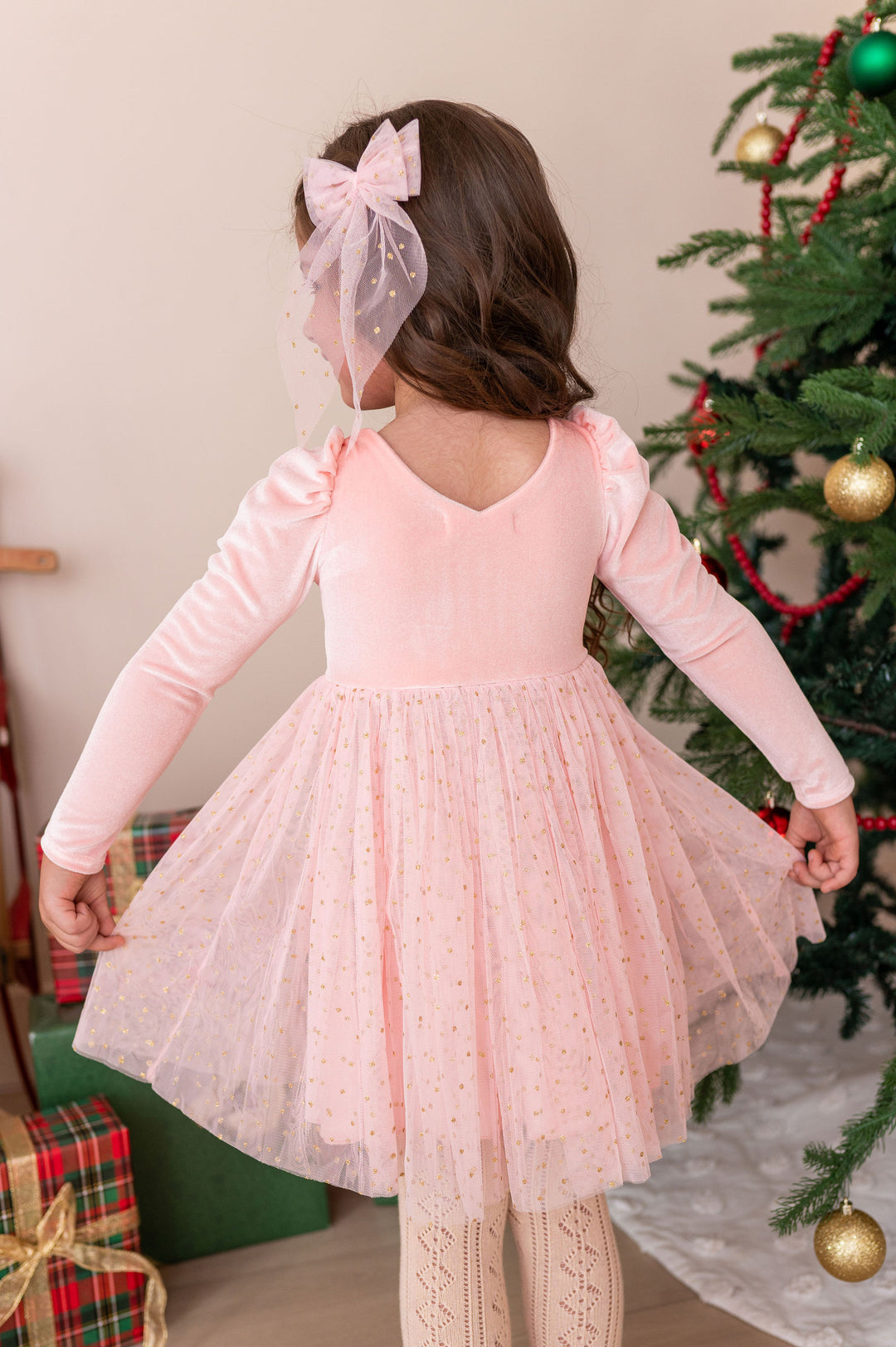 back view of girl wearing light pink fancy christmas dress with sparkly gold dotted tulle skirt and matching hair bow
