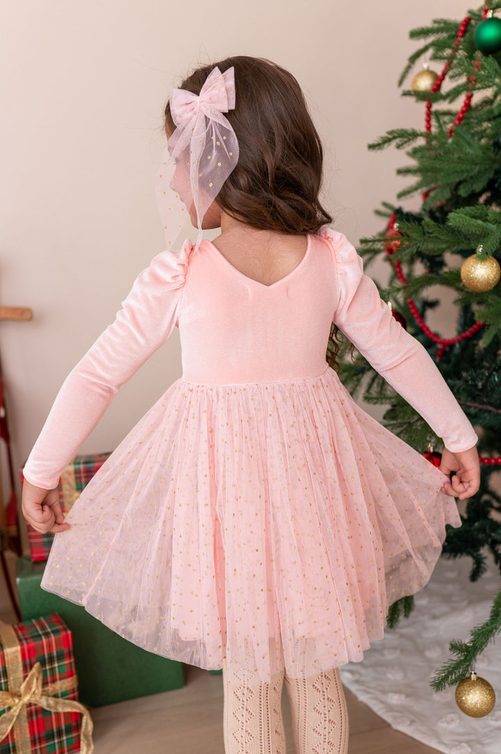 back view of girl wearing light pink fancy christmas dress with sparkly gold dotted tulle skirt and matching hair bow