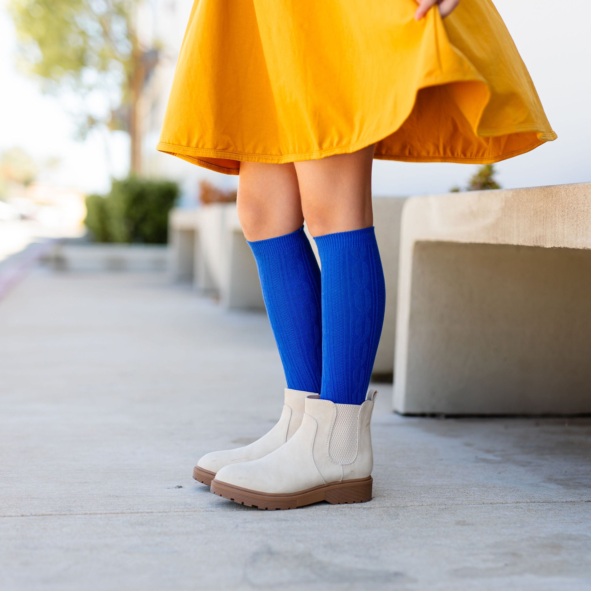 little girl standing in mustard yellow dress wearing bright blue cable knit knee high socks