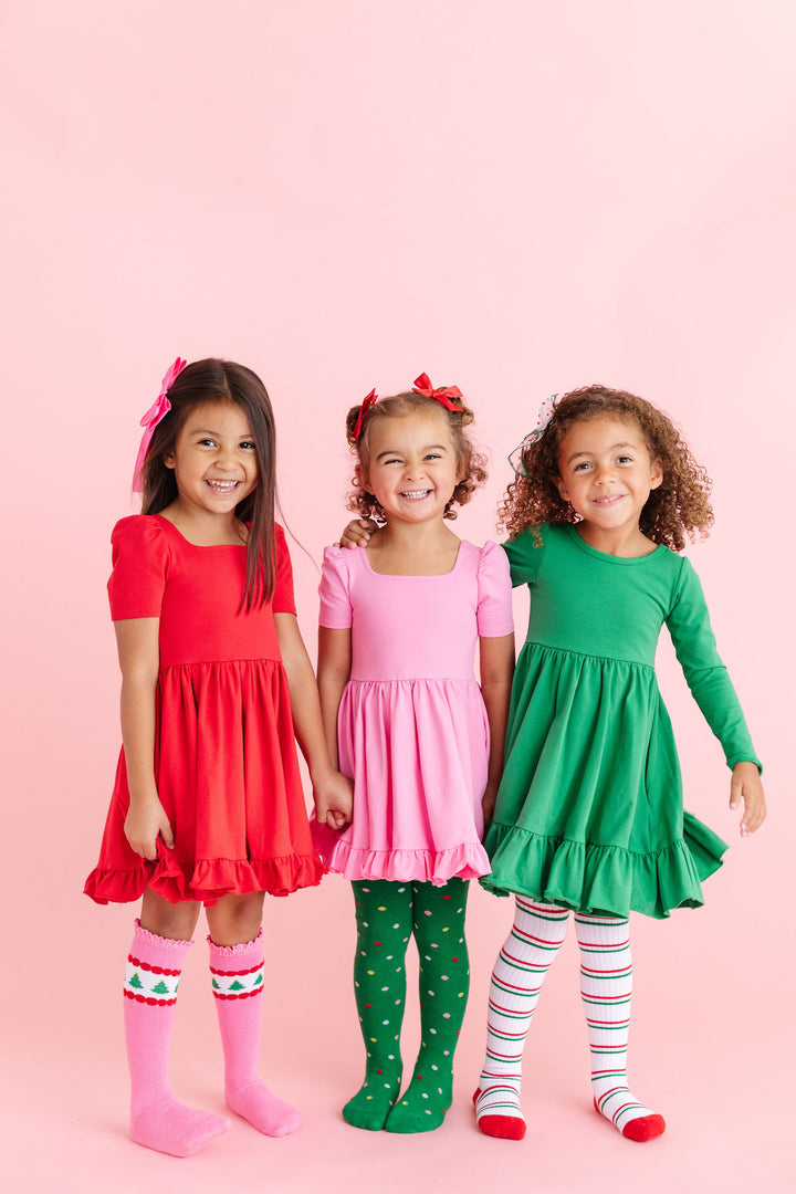 little girls in playful red, pink and green twirl dresses with matching Christmas bows and patterned tights and knee highs