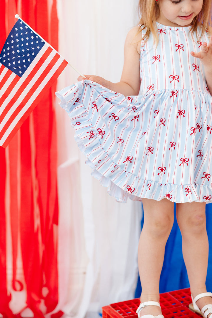girl in sleeveless twirl dress with white, blue and red stripe with dainty red bow print for 4th of July