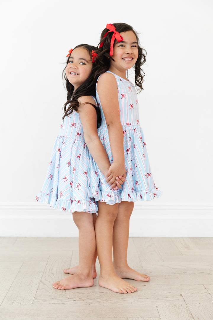 sisters in matching sleeveless twirl dress with white, blue and red stripe with dainty red bow print for 4th of July