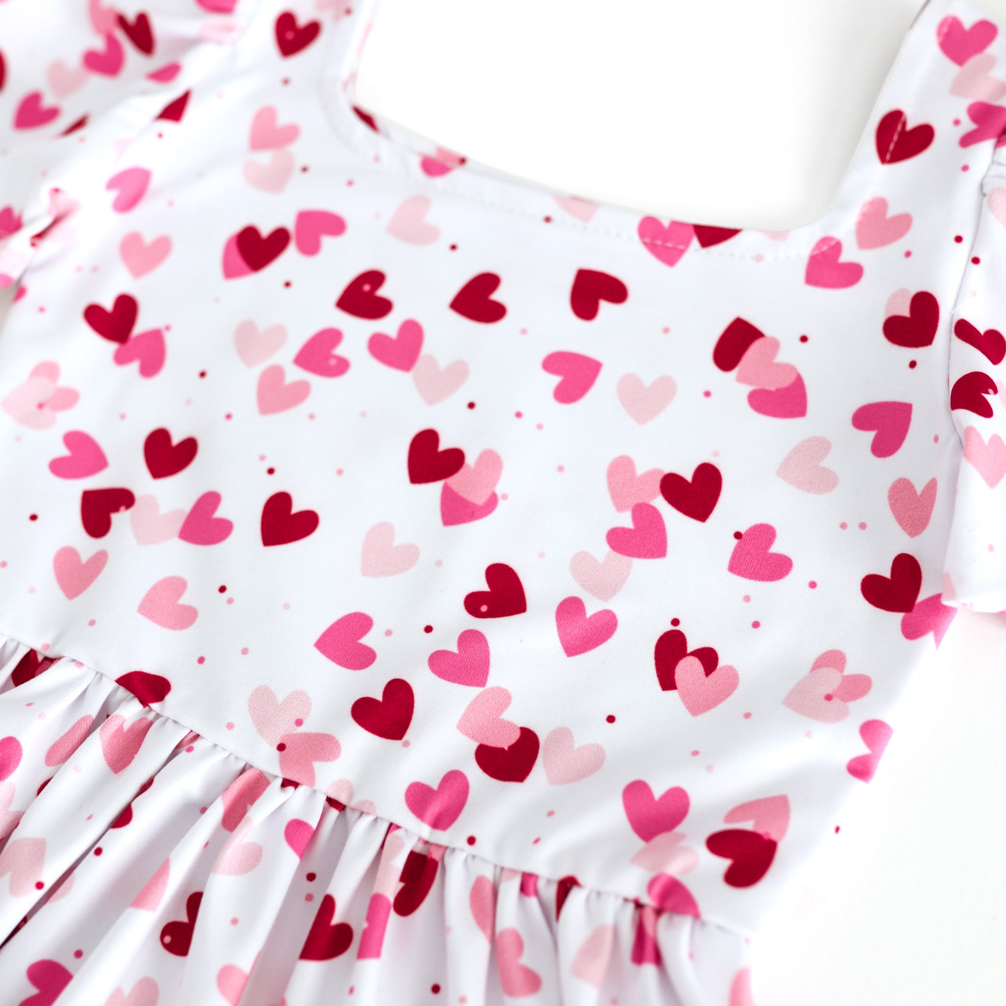 closeup of confetti heart print in shades of pink and red on white base twirl dress bodice