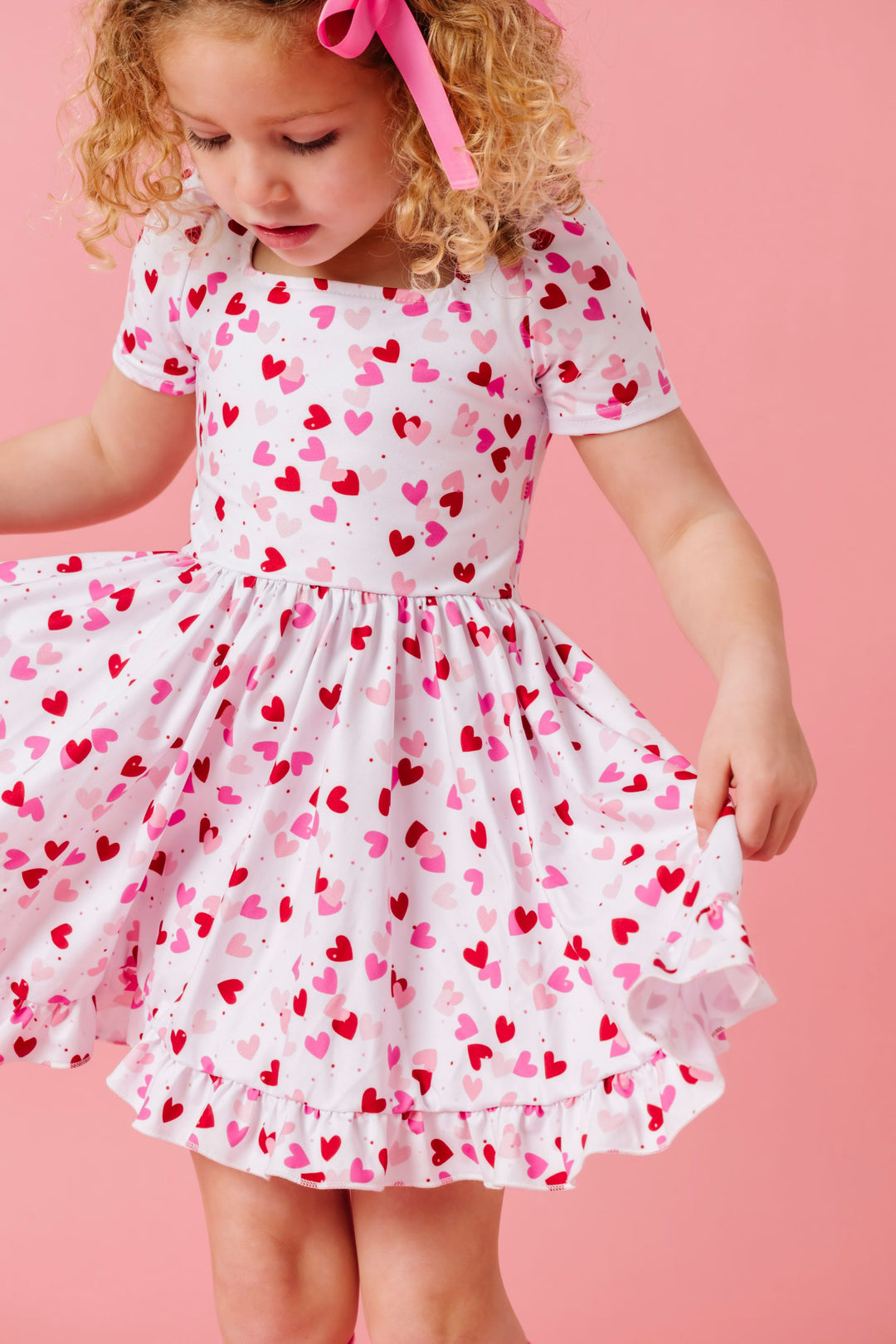 young girl in white Valentine's themed dress with scattered hearts print in shades of pink and red