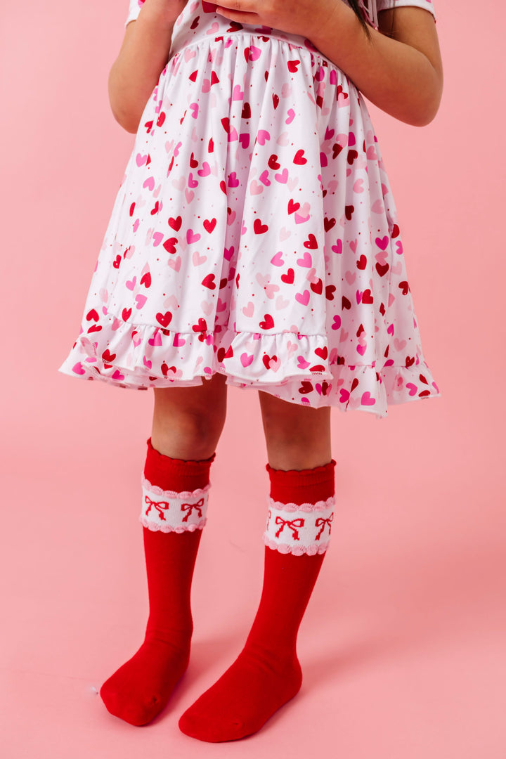 girl in white twirl dress with red and pink confetti hearts paired with bright red knee socks with bow design