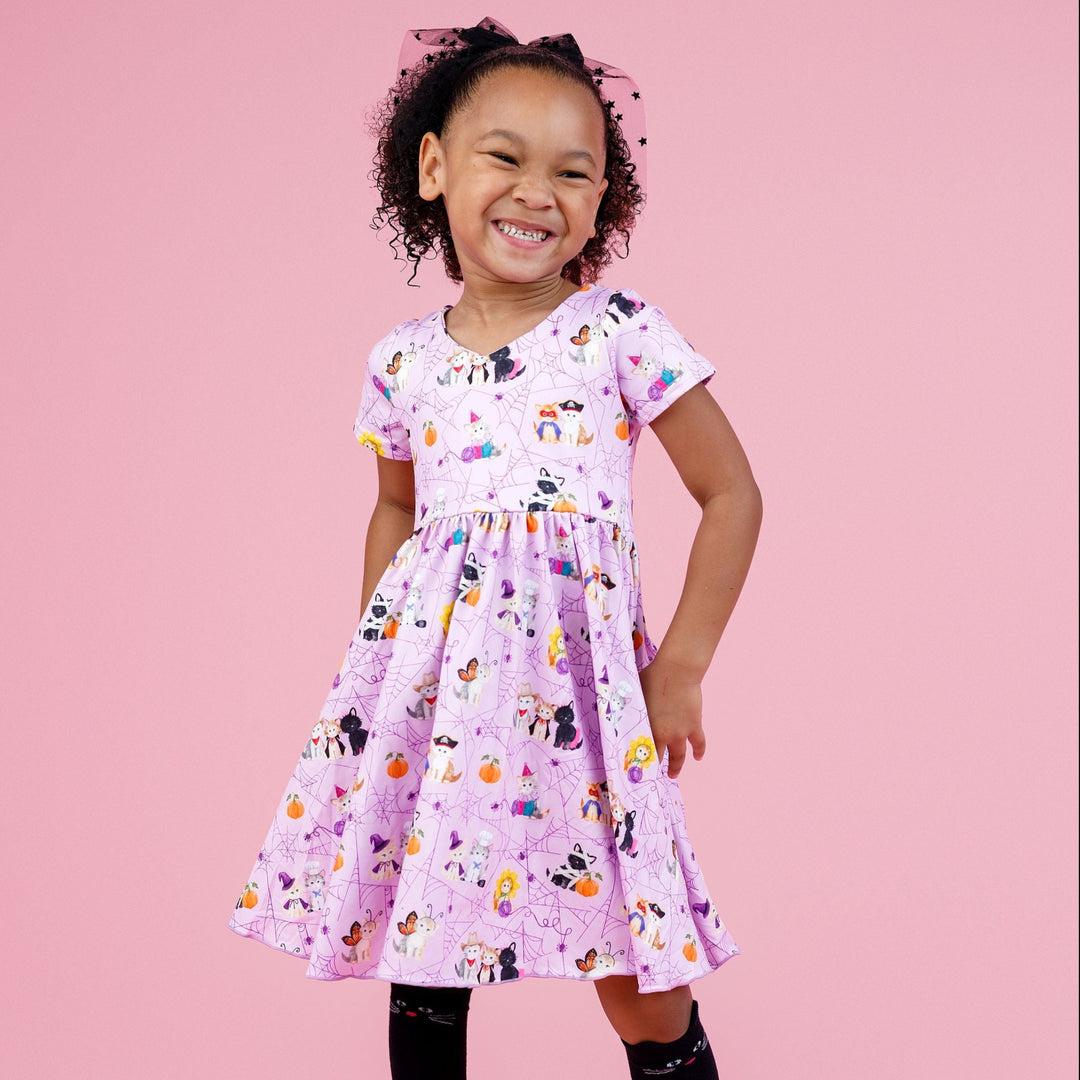 little girl in lavender v-neck twirl dress with purple spider web and kittens wearing Halloween costumes print paired with black cat knee socks and sheer black star hair bow