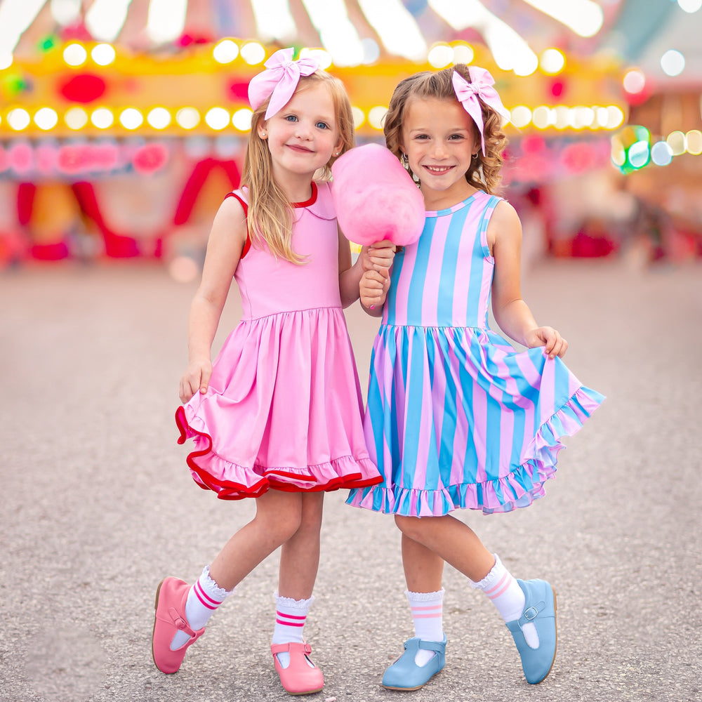 two little girls standing at a carnival in cute carnival themed twirl dresses and matching pink hair bows