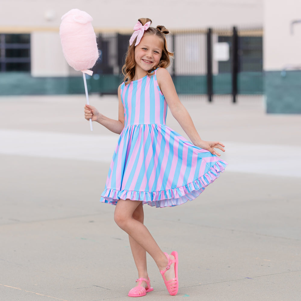 little girl in cotton candy striped dress holding large pink cotton candy treat