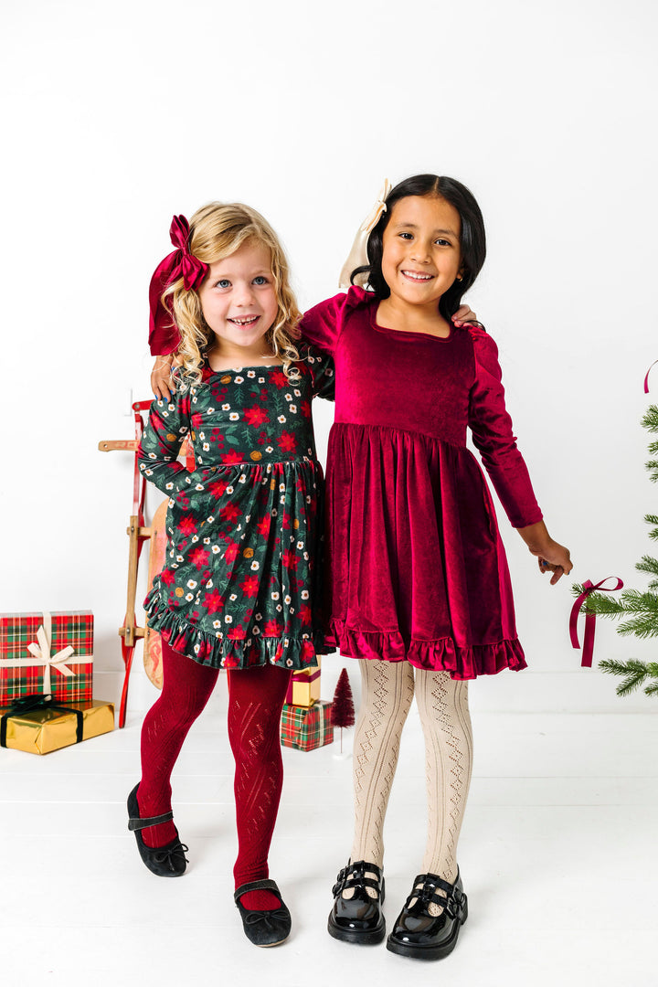 two girls in long sleeve velvet Christmas dresses in cranberry red and poinsettia print with matching tights and bows