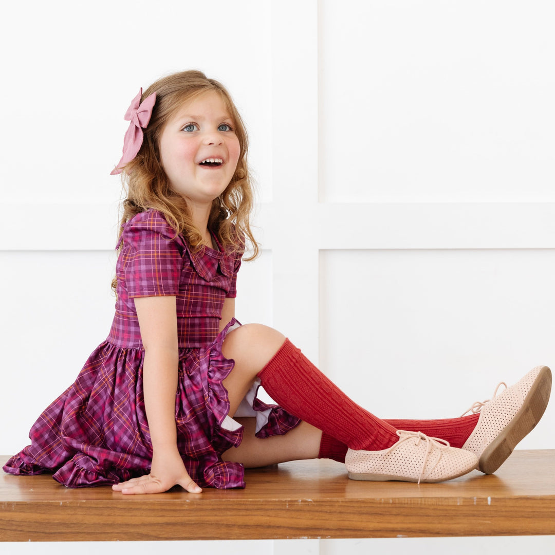little girl sitting on bench in cranberry plaid twirl dress