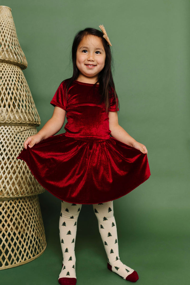 girl in cranberry red velvet top and skirt paired with Christmas tree tights and gold sparkly bow