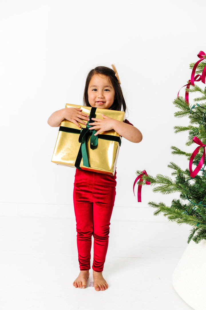 little girl holding Christmas gift in deep red velvet leggings