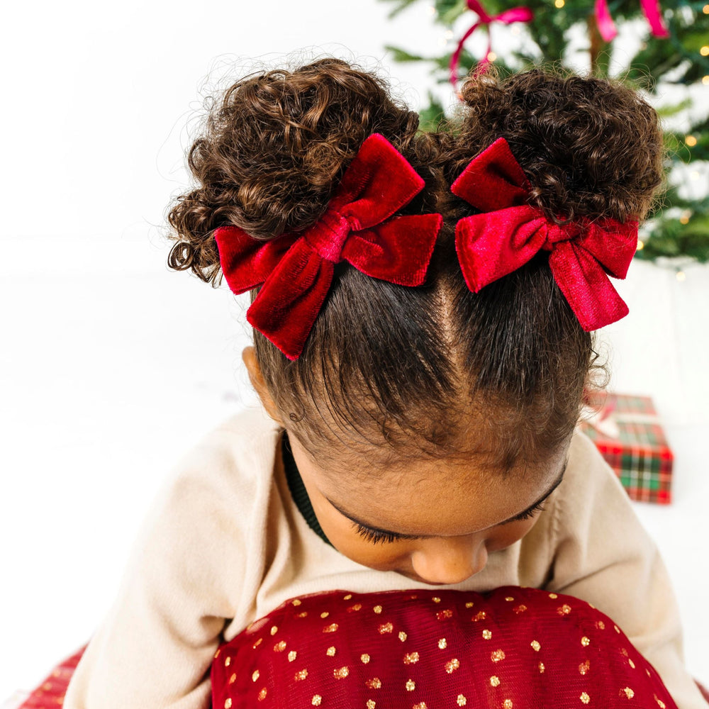 little girl in cream and cranberry Christmas outfit with matching velvet pigtail bows on clips