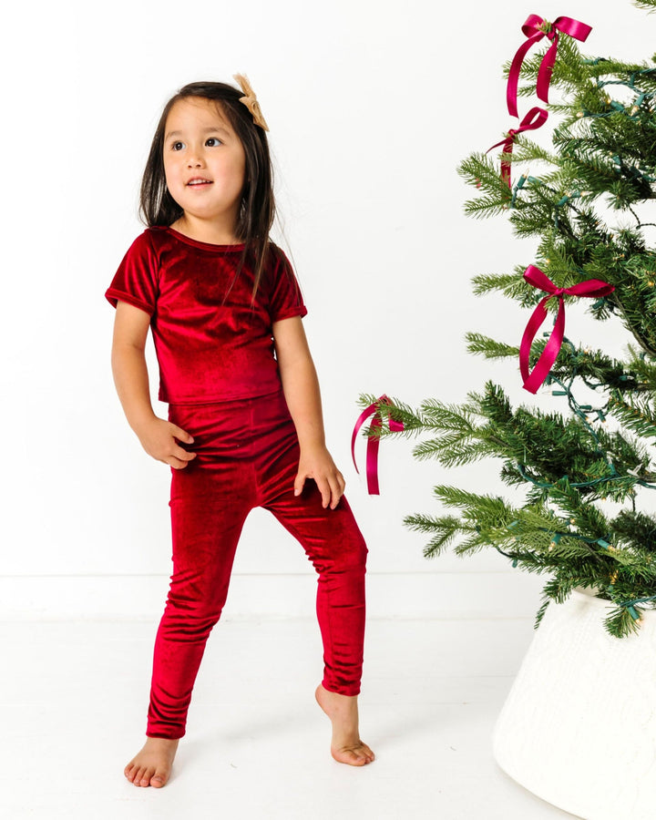 little girl by Christmas tree with deep red velvet top and leggings