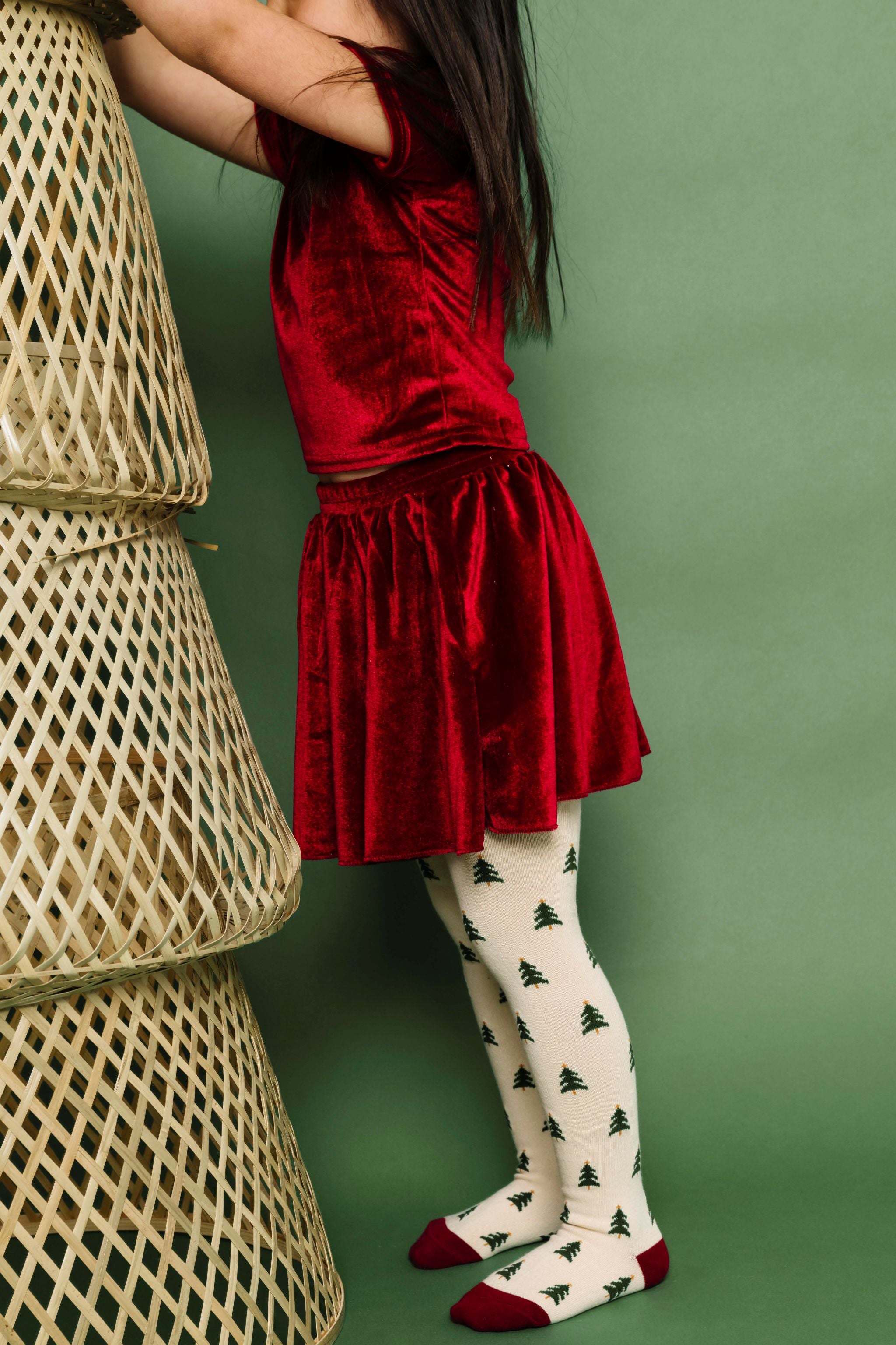 little girl in matching cranberry red velvet top and skirt paired with cream Christmas tree knit tights
