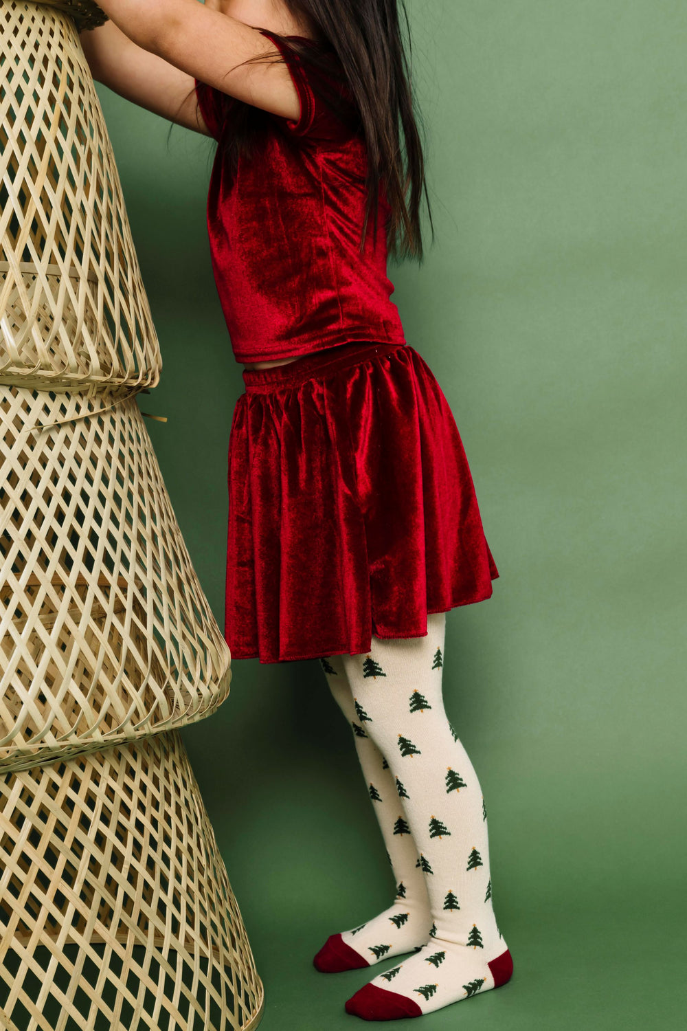 little girl in matching cranberry red velvet top and skirt paired with cream Christmas tree knit tights