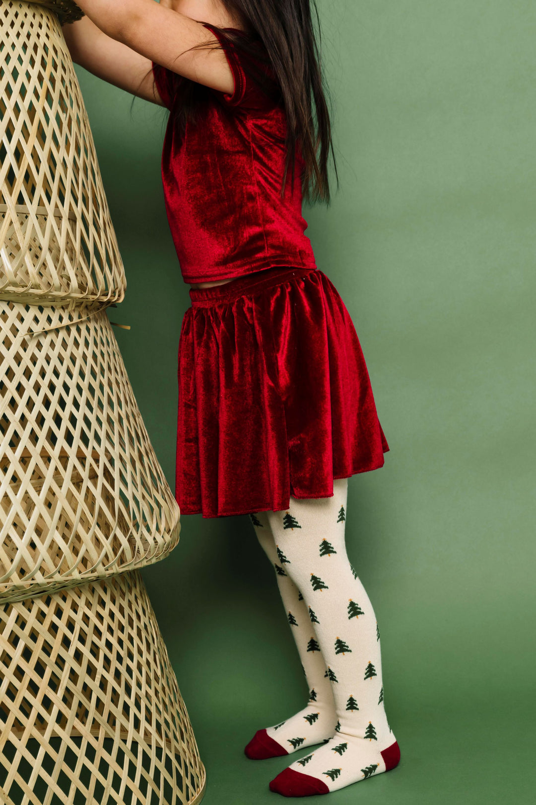 little girl in matching cranberry red velvet top and skirt paired with cream Christmas tree knit tights