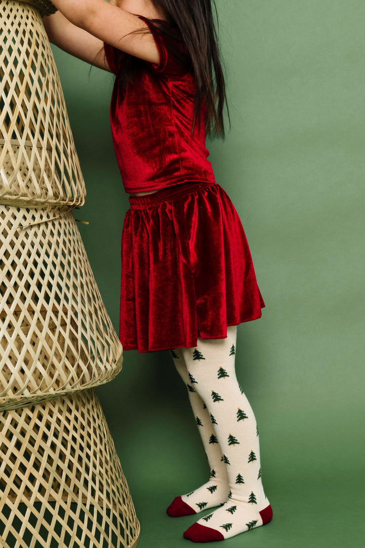 little girl in matching cranberry red velvet top and skirt paired with cream Christmas tree knit tights