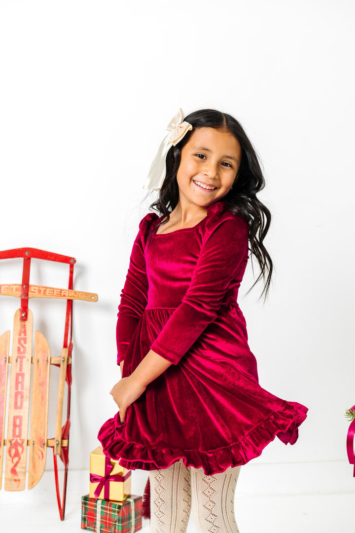 girl twirling by sled in deep red long sleeve velvet twirl and cream open knit tights