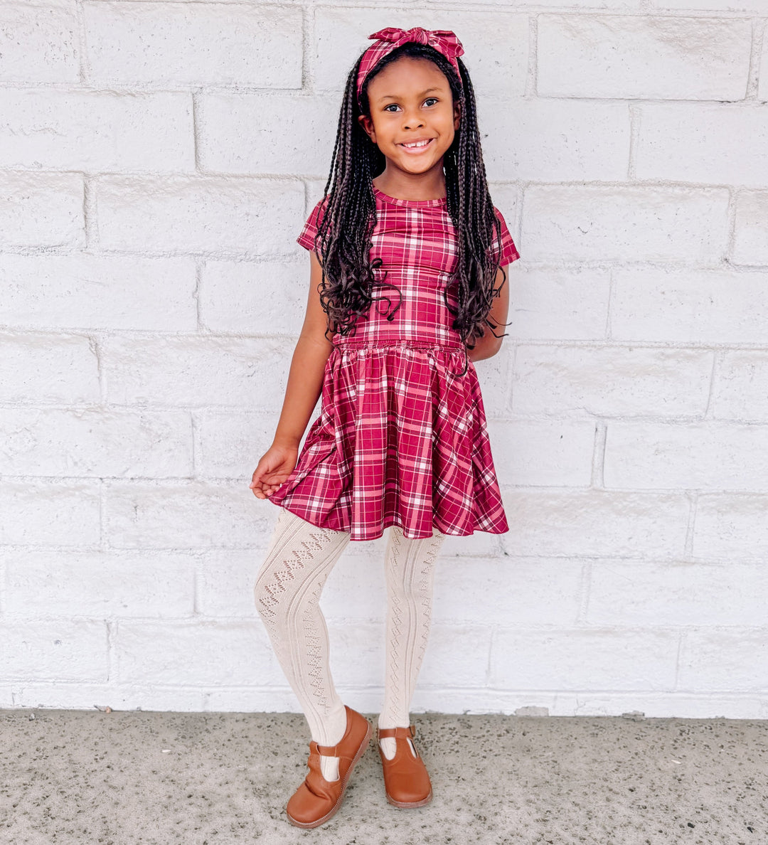 girl in crimson red plaid top, matching skirt and headband paired with cream pointelle tights and brown mary janes