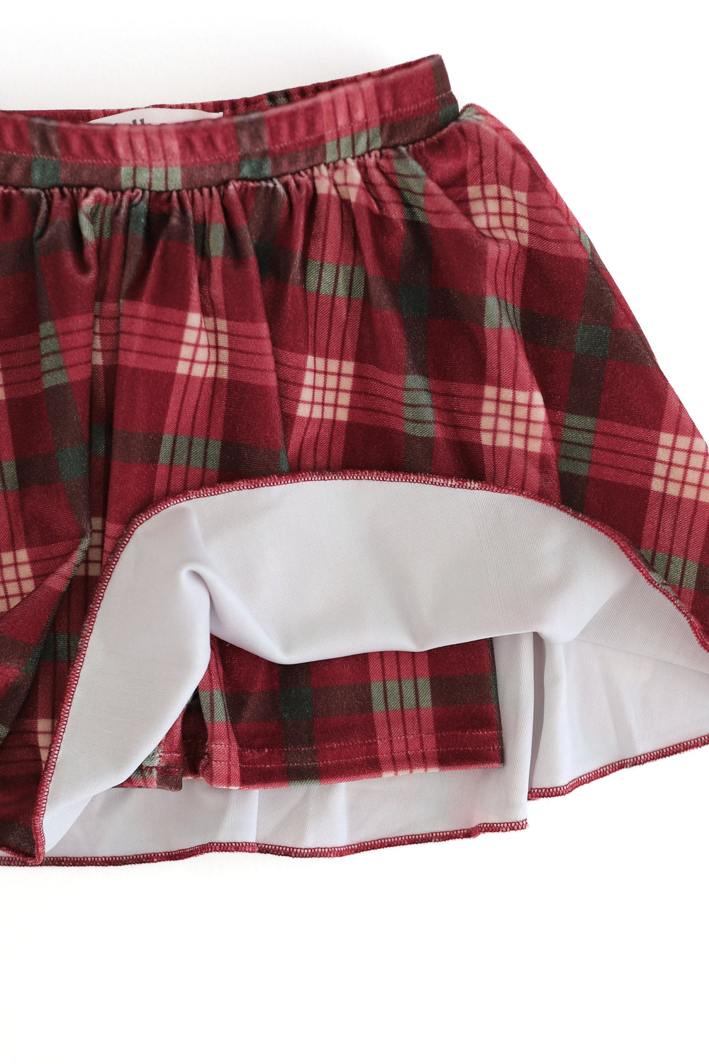 A close-up of a plaid velvet skort in crimson, green, and cream, with the hem turned up to show built in matching velvet shorts