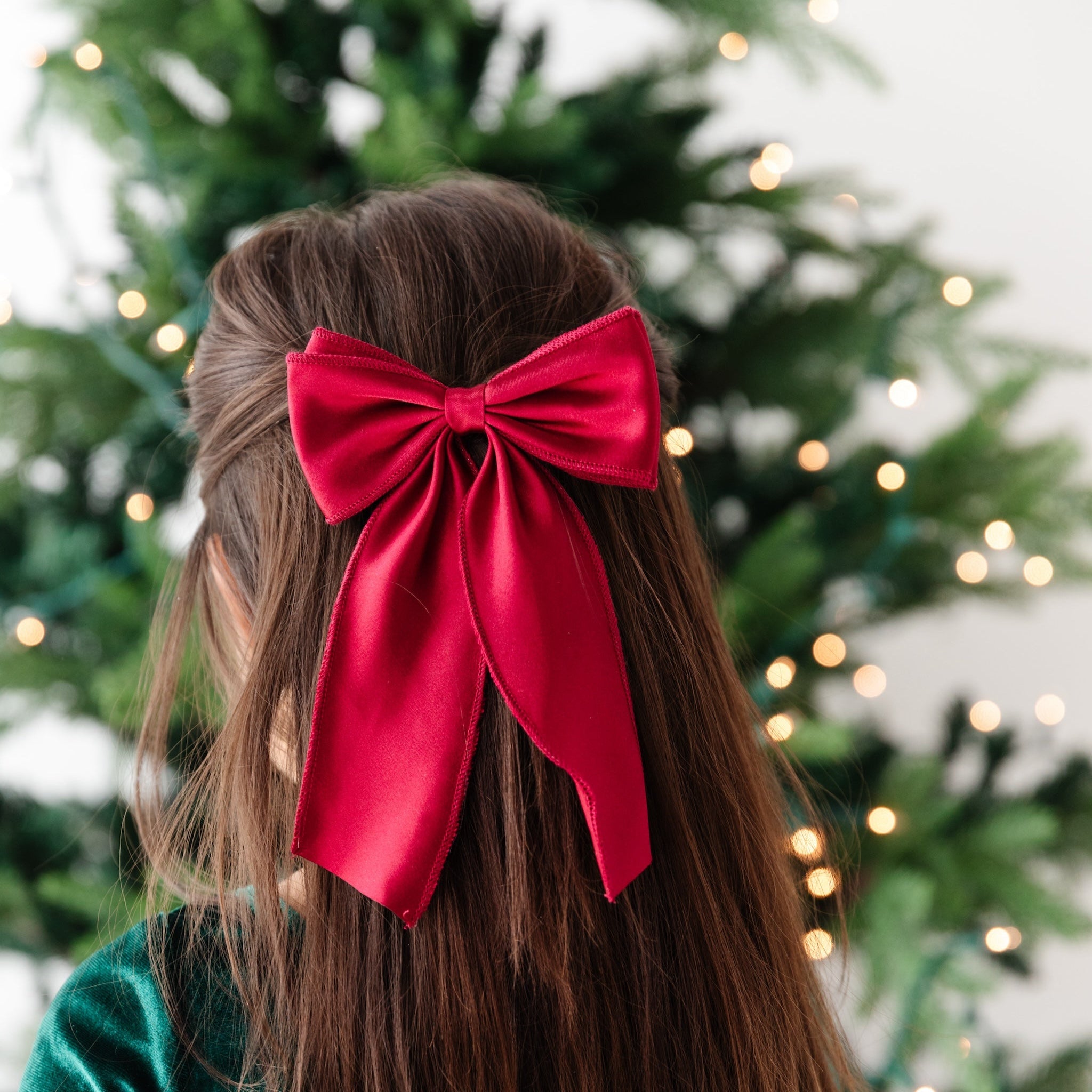 little girl looking at Christmas tree in deep red satin bow on clip