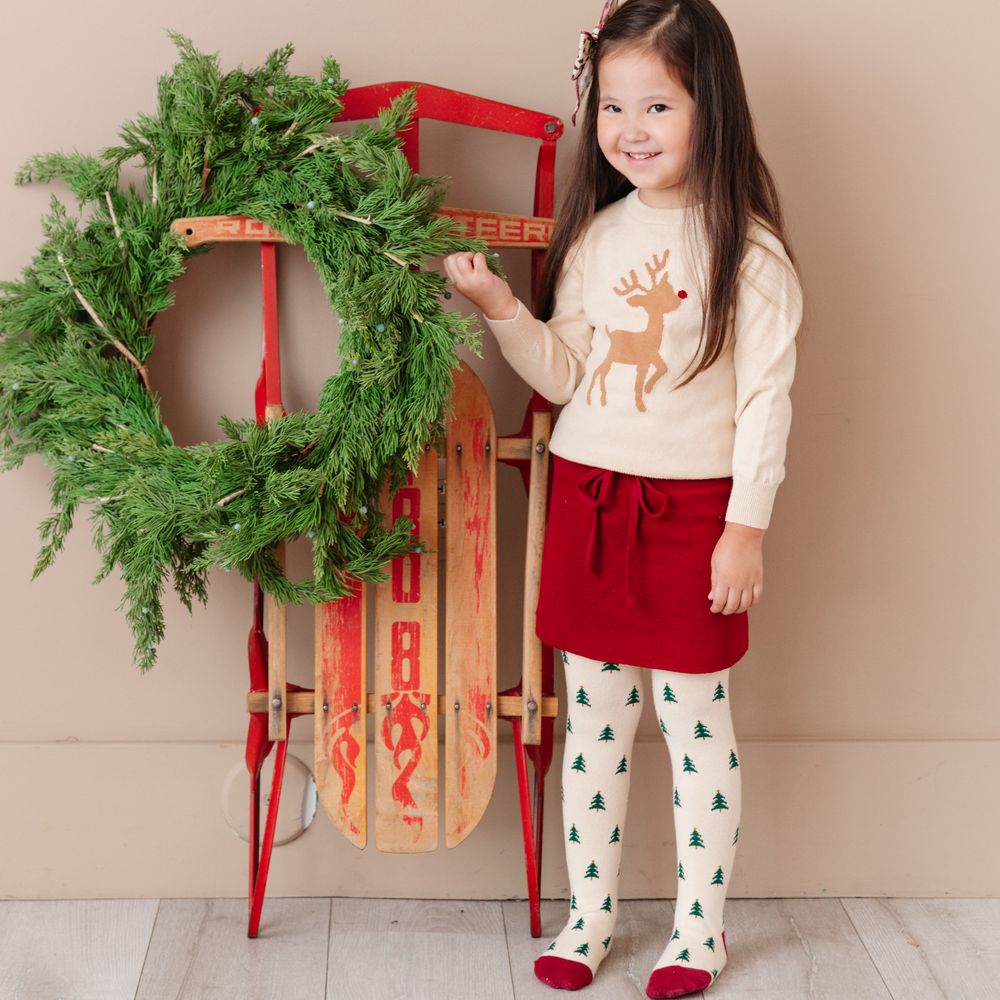 girl in christmas outfit with crimson red knit skirt, rudolph sweater and tree tights