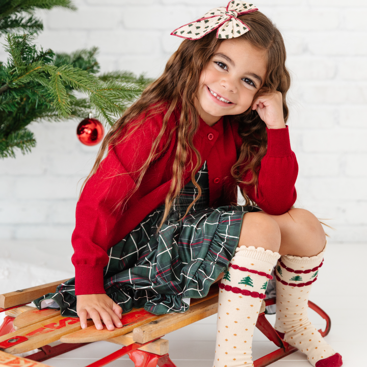 girl in crimson red cardigan sweater with christmas outfit sitting on sled