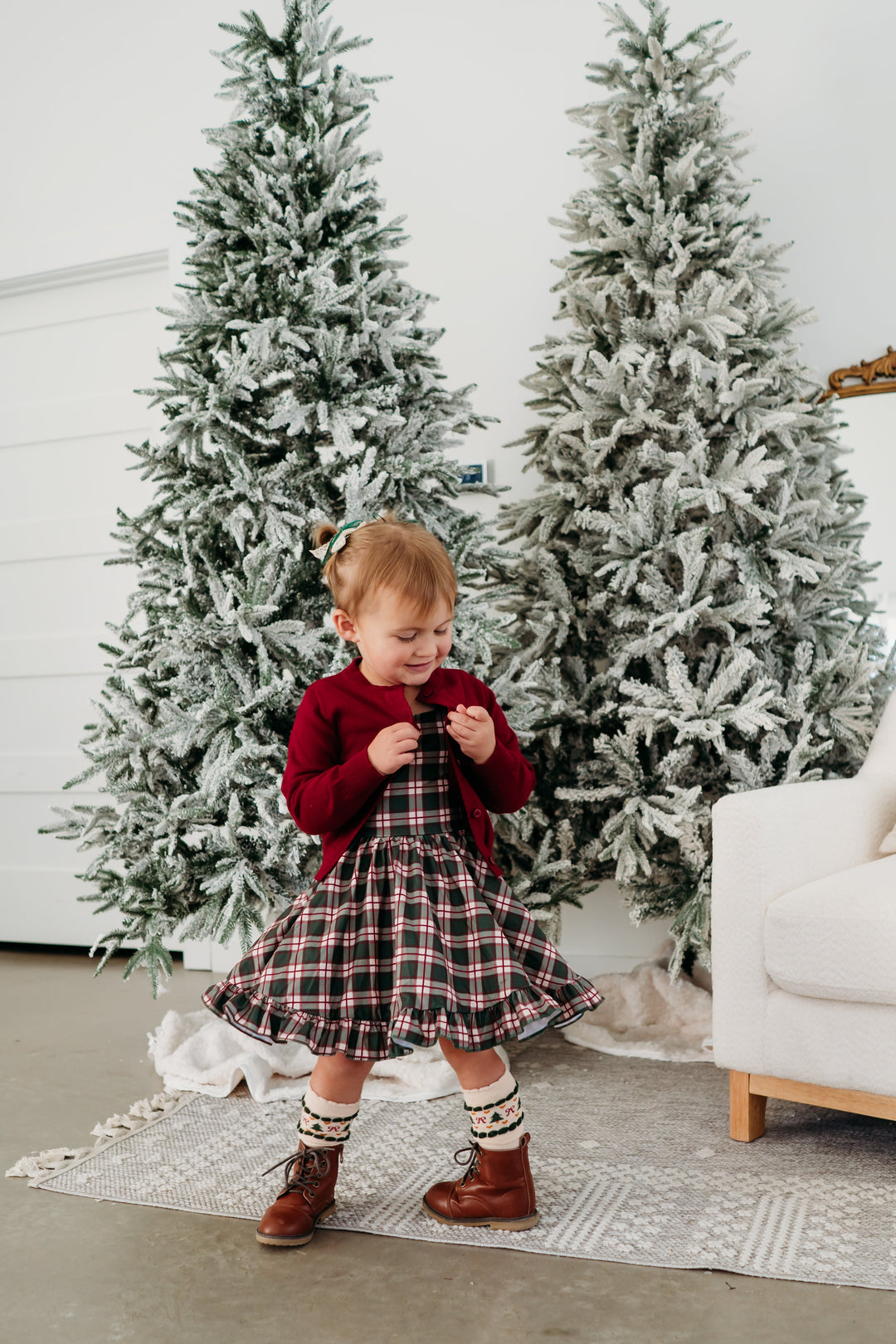 little girl twirling in front of Christmas trees in forest green plaid twirl dress paired with cream fair isle knee socks and crimson red cotton knit cardigan