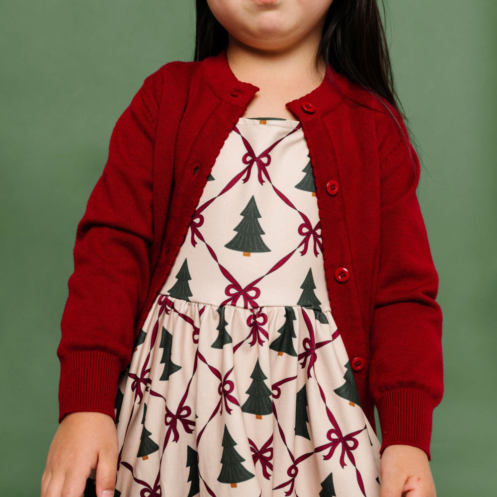 little girl in Christmas tree and bow print twirl dress with deep red cotton knit cardigan