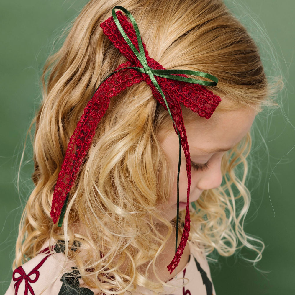 young girl in Christmas tree and bow print twirl dress paired with long tail crimson lace bow with green ribbon accent