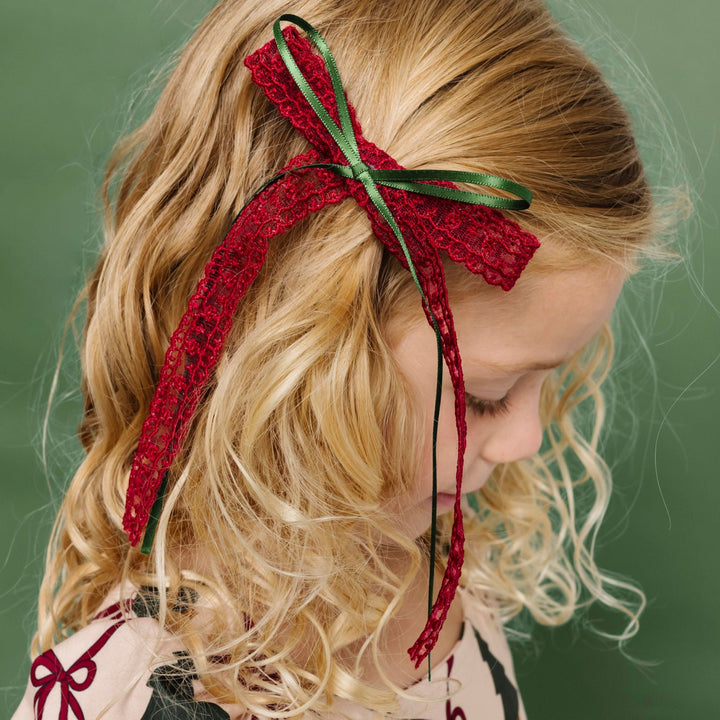 young girl in Christmas tree and bow print twirl dress paired with long tail crimson lace bow with green ribbon accent