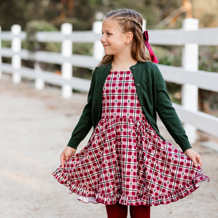 little girl in red gingham Christmas tree print twirl dress and matching green knit cardigan with red satin bow and tights