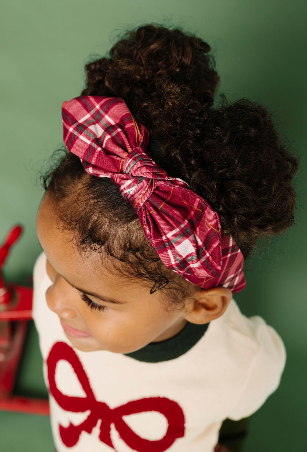 little girl in Christmas bow sweater paired with matching crimson plaid bow headband 