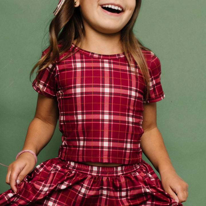 little girl in crimson plaid Christmas top and matching skirt paired with cream fair isle print knee socks