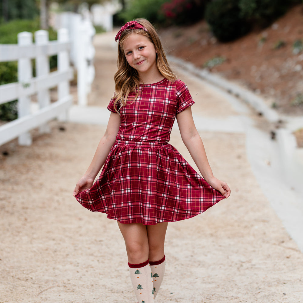 young girl in matching headband, top and skirt in crimson plaid paired with Christmas tree print knee high socks
