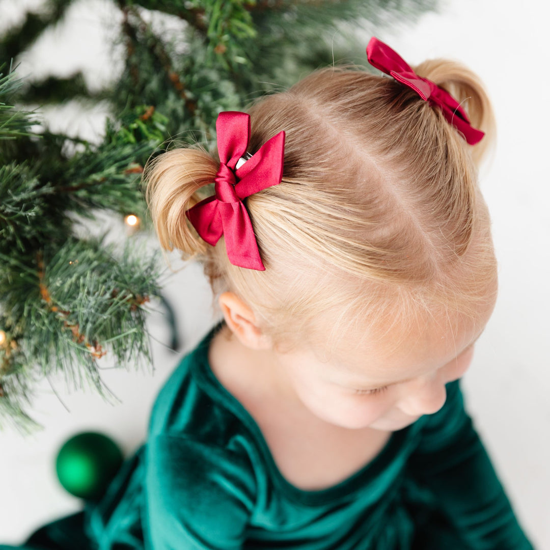 little girl in red satin pigtail bows and forest green velvet holiday dress in front of Christmas tree