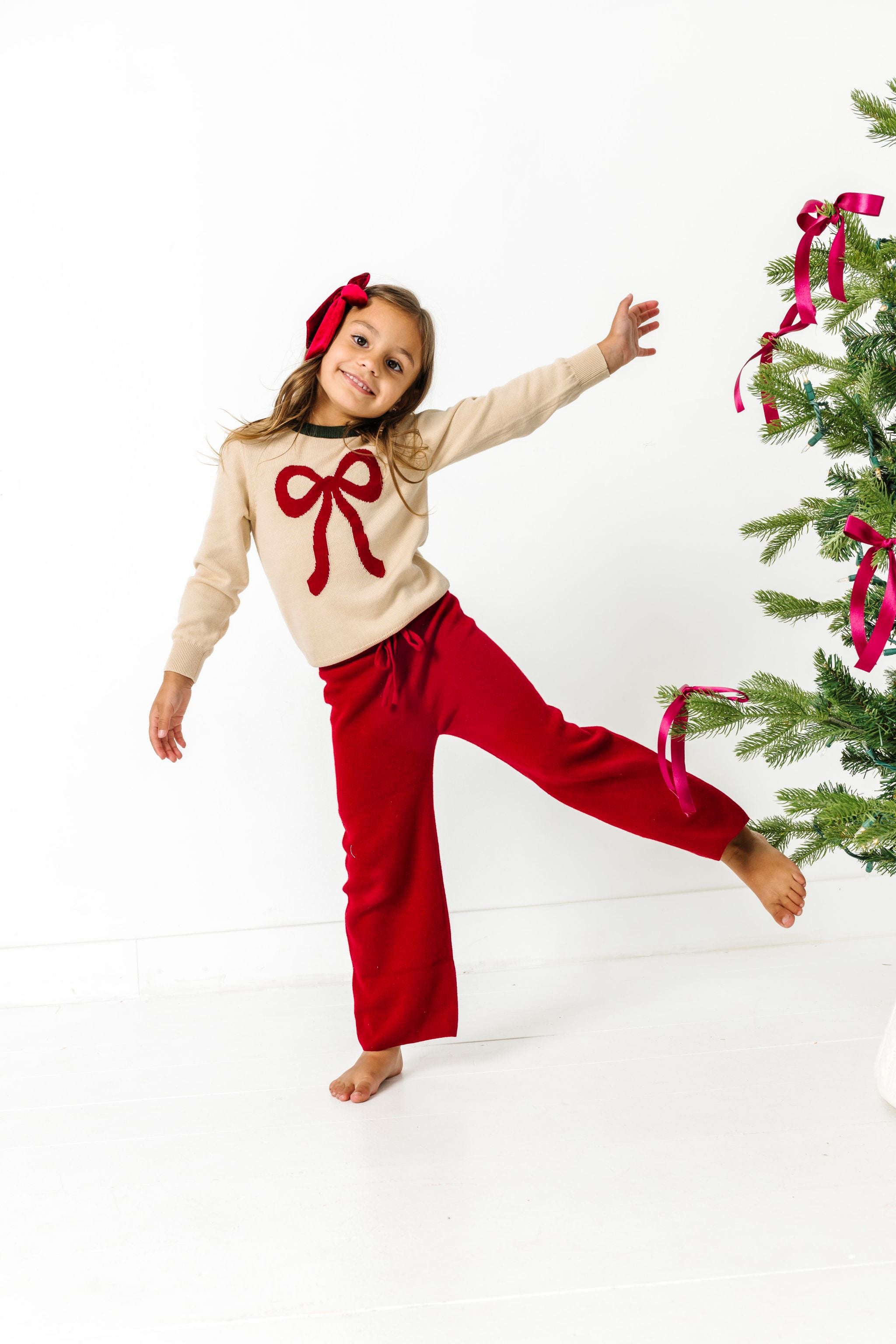 little girl in cream bow sweater and matching crimson sweater pants with velvet crimson hair bow