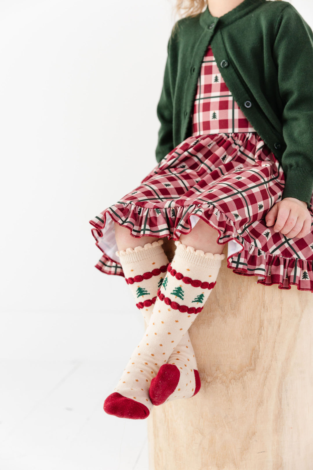 little girl in tree farm inspired Christmas knee highs and coordinating red gingham dress and forest green sweater