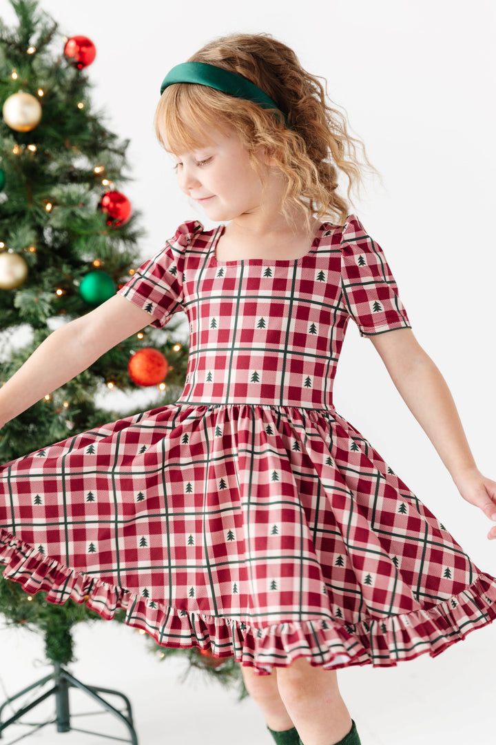 littler girl twirling in front of Christmas tree with red gingham dress and forest green socks and satin headband