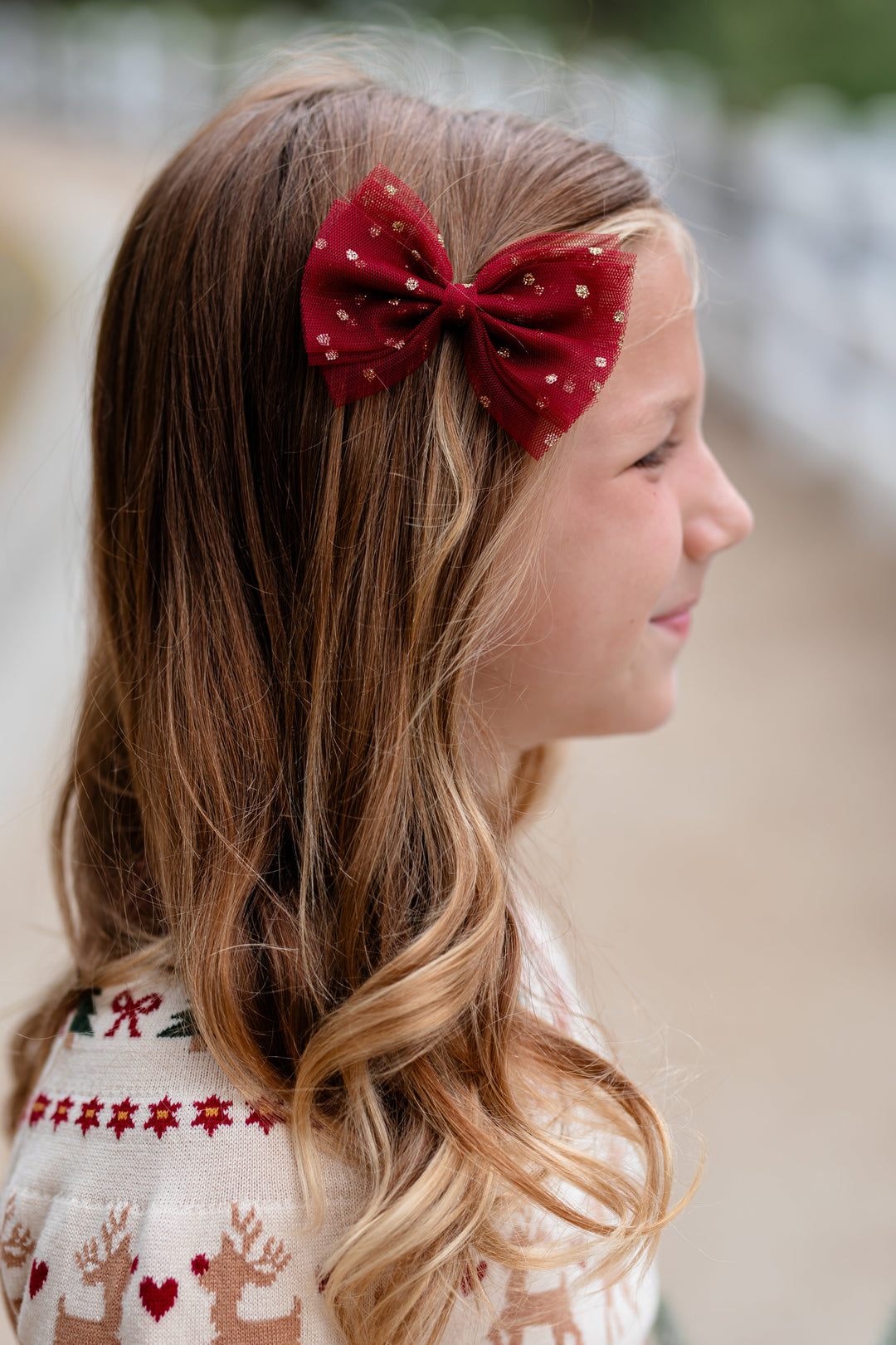 little girl in Christmas fair isle sweater paired with matching crimson tulle bow with gold sparkles