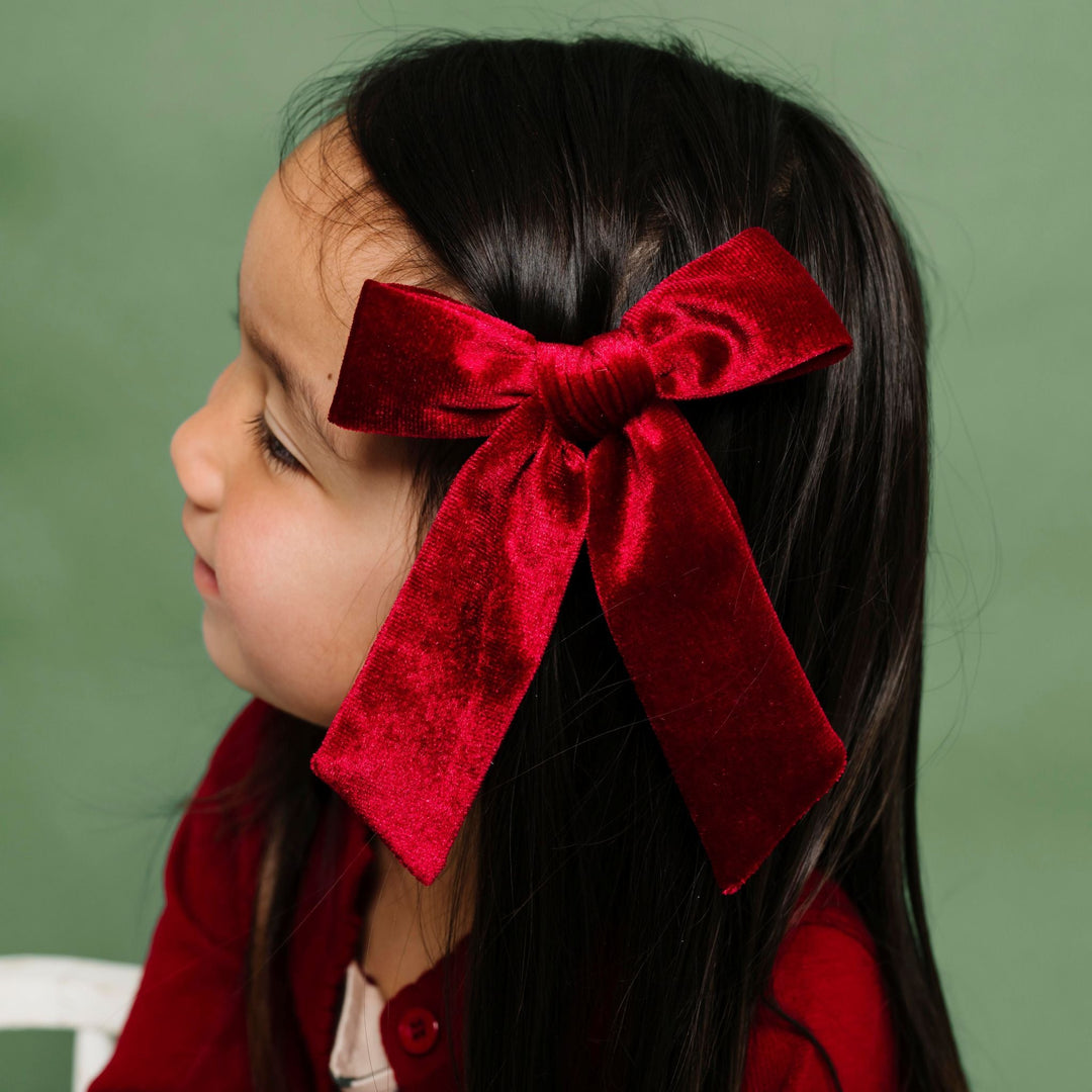 little girl in Christmas dress and crimson cardigan paired with crimson velvet bow on clip