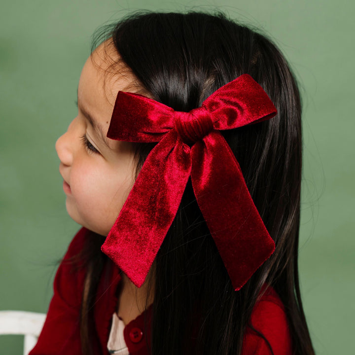 little girl in Christmas dress and crimson cardigan paired with crimson velvet bow on clip