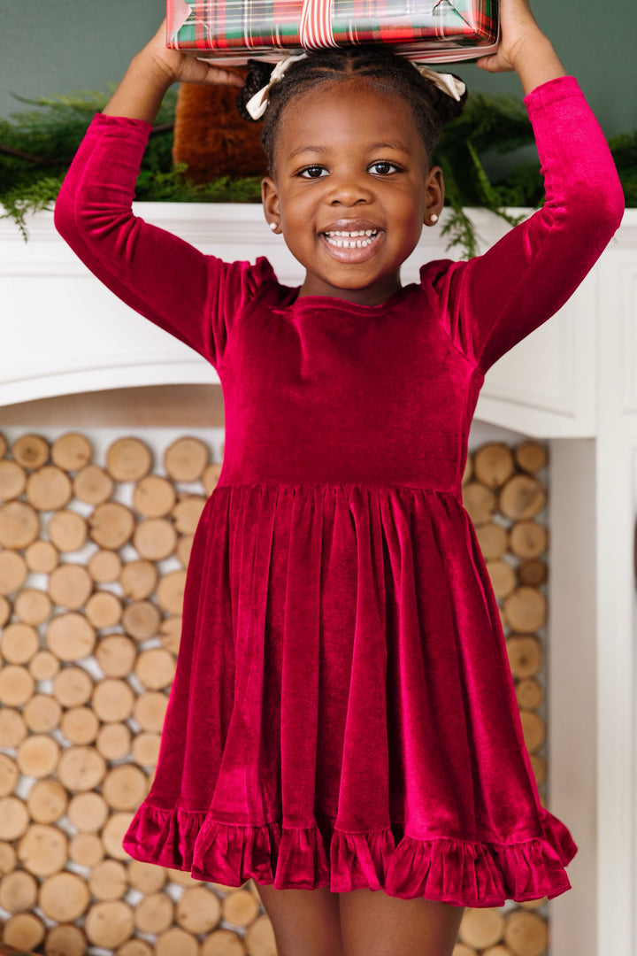 little girl holding Christmas gift in deep red velvet long sleeve twirl dress