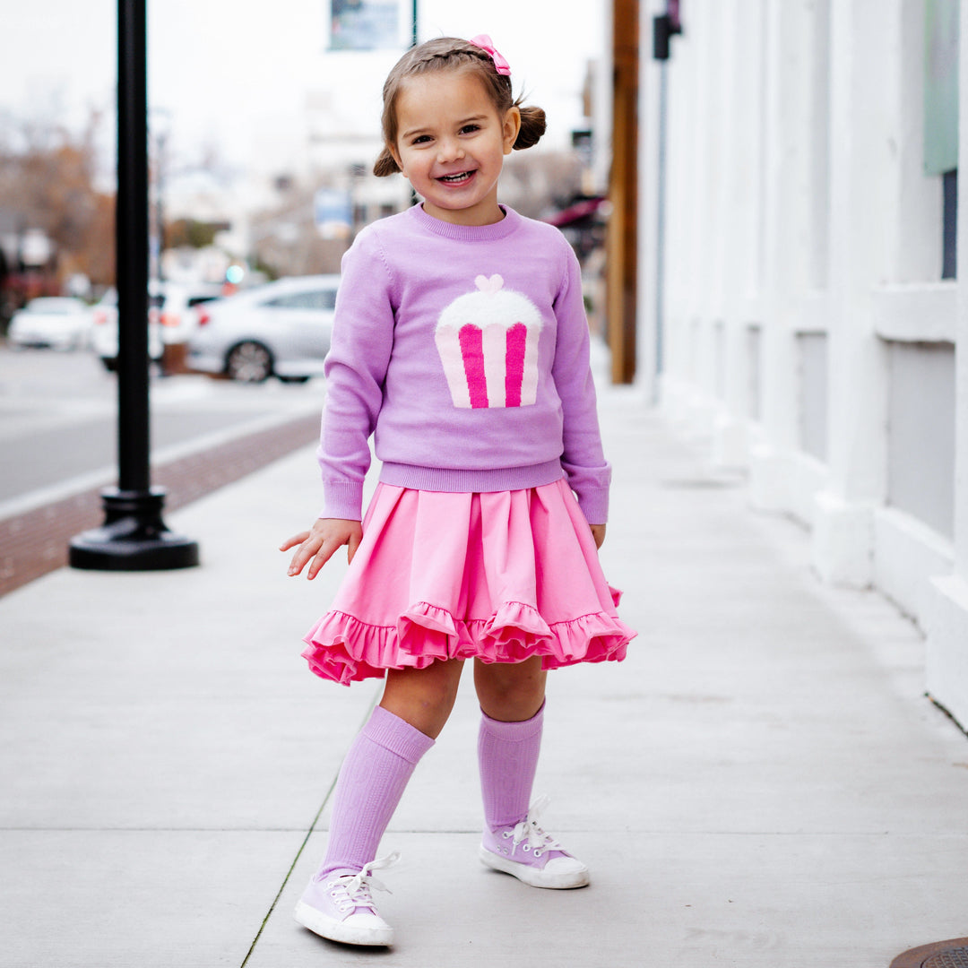 little girl in lavender pullover sweater with cupcake design, pink twirl dress and matching lavender cable knit knee highs