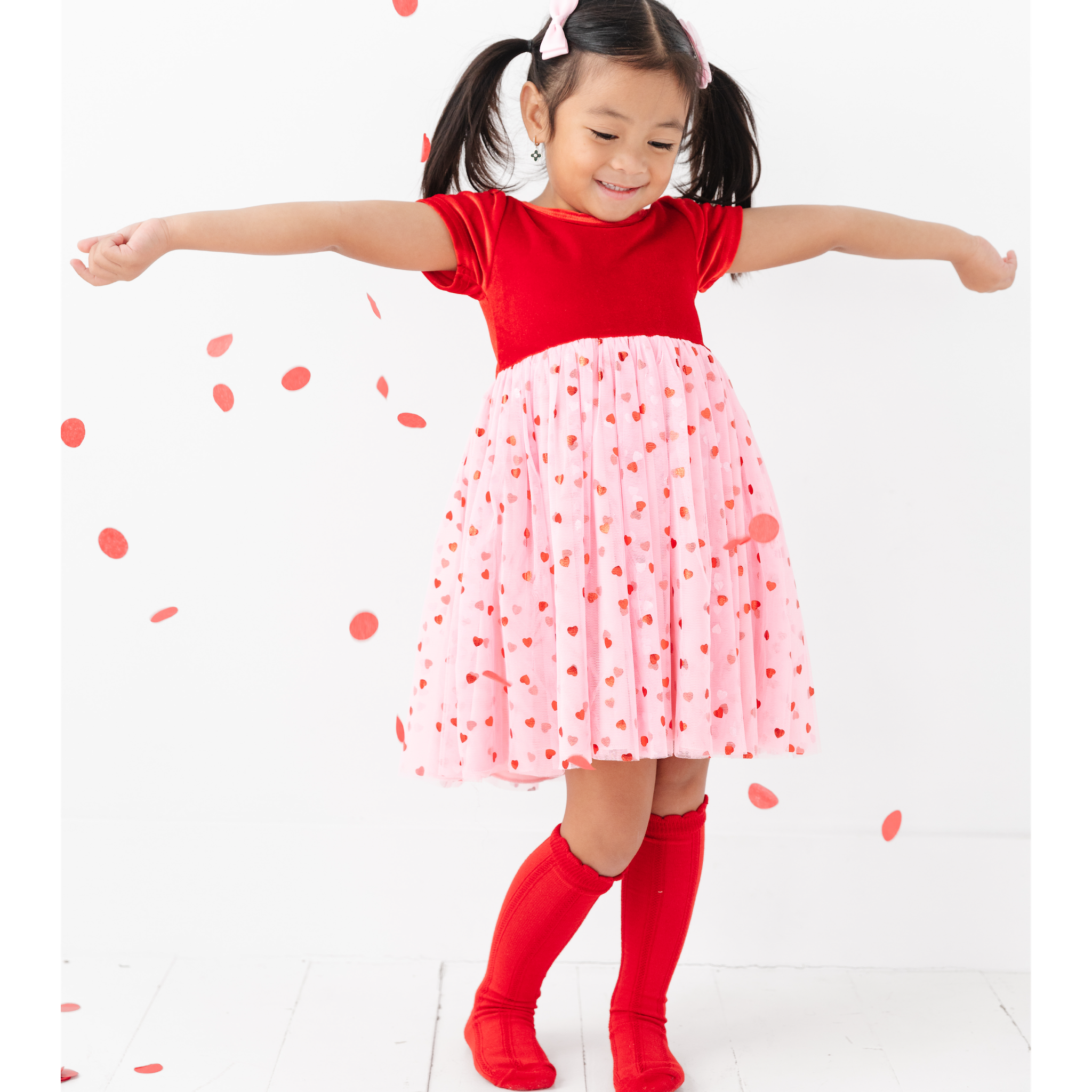 girl wearing valentine's day fancy dress with velvet and tulle and red hearts throwing confetti