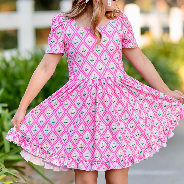 girl in pink dress with diamond pattern and daisy print 